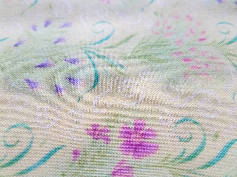 May include: A light yellow fabric featuring a repeating pattern of purple and pink flowers, green leafy stems, and thin white swirling lines. The textile has a visible woven texture with a soft, matte finish across the entire surface area.