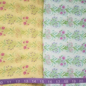 May include: Two pieces of fabric featuring a floral pattern with green vines and pink flowers. The left fabric has a yellow background, while the right fabric has a white background. A purple measuring tape is visible at the bottom, showing 22 inches.