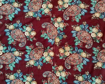 May include: A fabric featuring a repeating pattern of paisley motifs and clusters of cream-colored roses with green leaves set against a deep burgundy background. The design includes intricate floral details and curved shapes.