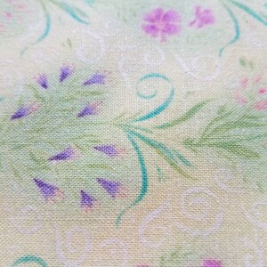 May include: A light yellow fabric featuring a repeating pattern of green leafy stems, small purple flower clusters, and delicate white swirling line designs. The textile has a visible woven texture with a soft, matte finish throughout the surface.