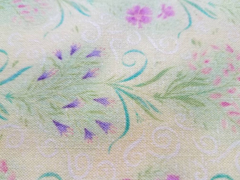 May include: A light yellow fabric featuring a repeating pattern of green leafy stems, small purple flower clusters, and delicate white swirling line designs. The textile has a visible woven texture with a soft, matte finish throughout the surface.