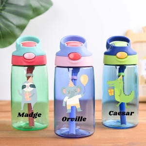 May include: Three colorful water bottles with animal graphics. One has a sloth, another an elephant holding a balloon, and the last a crocodile. Each bottle has a name: Madge, Orville, and Caesar. The bottles have a straw and a flip-top lid.