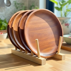 Könnte beinhalten: Ein Set aus fünf runden Holzplatten in einem Holzregal. Die Platten haben eine warme braune Farbe mit sichtbarer Holzmaserung. Das Regal ist aus hellem Holz gefertigt und hat ein schlichtes, minimalistisches Design. Die Platten haben einen Durchmesser von etwa 25 cm.