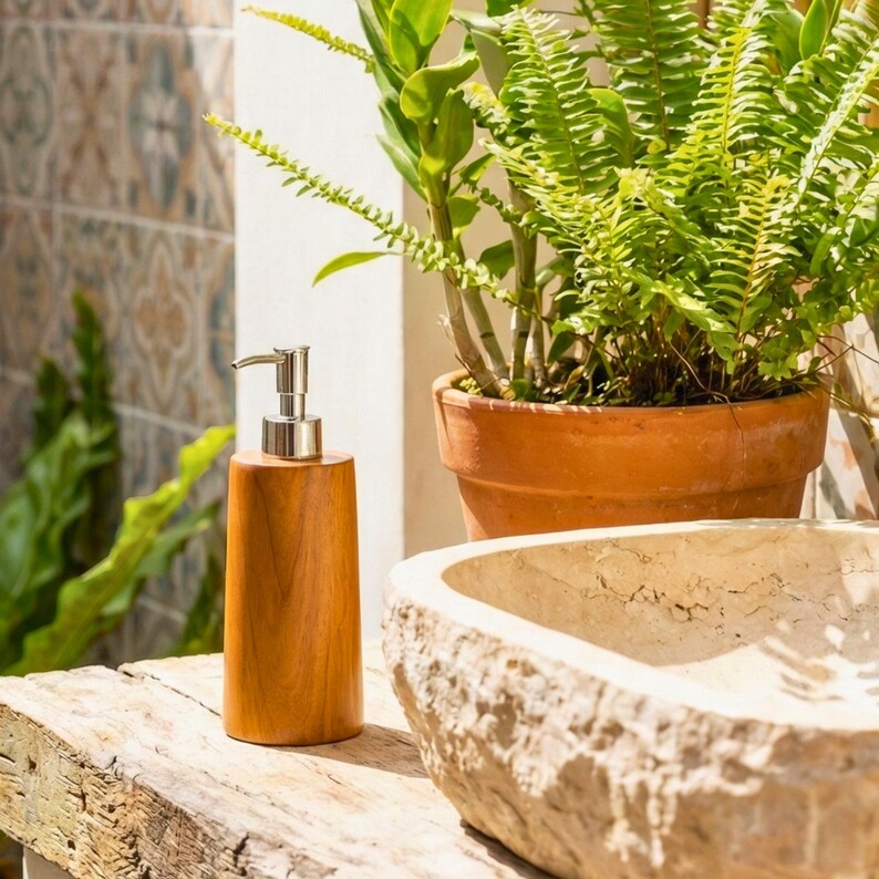 May include: A wooden soap dispenser with a silver pump sits on a weathered wooden surface. The dispenser is cylindrical and has a natural wood grain finish. A stone sink and potted plants are in the background, creating a spa-like atmosphere.