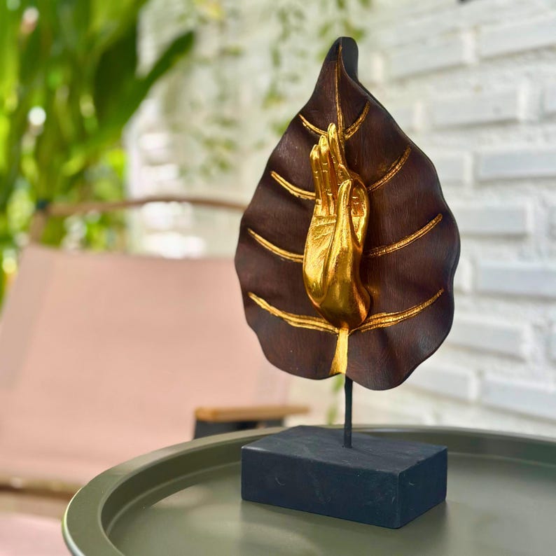 Pu&ograve; includere: Scultura decorativa con una mano dorata che emerge da una foglia marrone scuro con dettagli dorati. La foglia &egrave; montata su una base nera. Un oggetto di arredamento per la casa unico.