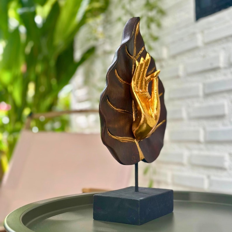 Pu&ograve; includere: Scultura in legno raffigurante una foglia marrone scuro con dettagli dorati e una mano dorata. La scultura &egrave; montata su una base rettangolare nera. Oggetto decorativo.