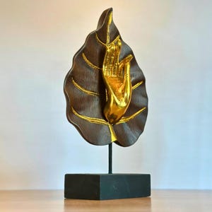 Pu&ograve; includere: Scultura decorativa con una mano color oro che emerge da una foglia marrone scuro con dettagli dorati. La foglia &egrave; montata su un supporto nero, creando un contrasto sorprendente. Un oggetto di arredamento unico.