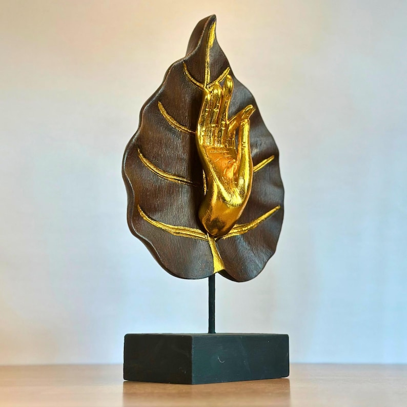 Pu&ograve; includere: Scultura decorativa con una mano color oro che emerge da una foglia marrone scuro con dettagli dorati. La foglia &egrave; montata su un supporto nero, creando un contrasto sorprendente. Un oggetto di arredamento unico.