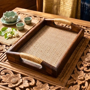 May include: A dark brown wooden serving tray with woven rattan handles and a chevron patterned base. The tray sits on a carved wooden surface. The tray's dimensions are approximately 40 cm x 30 cm.