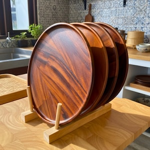 May include: A set of four round wooden serving trays with a rich, reddish-brown grain pattern. The trays are displayed in a wooden stand, showcasing their natural wood tones. The trays are ideal for serving food or as decorative pieces.
