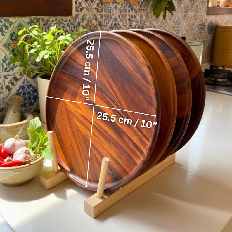 May include: A stack of four round wooden plates, each 10 inches in diameter, displayed in a wooden plate rack. The plates have a rich, dark brown wood grain pattern. The rack is made of light-colored wood.