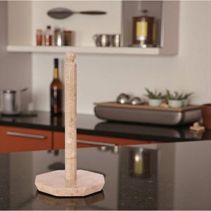 May include: A beige marble paper towel holder with a hexagonal base and a vertical post topped with a rounded finial. The kitchen accessory is made of natural stone and sits on a black countertop.