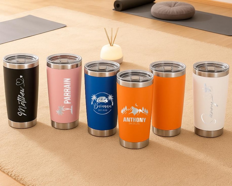 Puede incluir: Seis vasos aislados de acero inoxidable en negro, rosa, azul, naranja y blanco. Cada vaso tiene una tapa y una base plateadas. Los vasos est&aacute;n personalizados con nombres y gr&aacute;ficos, incluyendo un coraz&oacute;n, palmeras, una furgoneta camper y una monta&ntilde;a.
