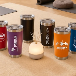 Puede incluir: Una colecci&oacute;n de vasos aislados en varios colores, incluyendo rojo, morado, negro, naranja y azul. Cada vaso tiene una tapa y base plateadas. Algunos vasos presentan textos y gr&aacute;ficos personalizados, como nombres y fechas, ideales para regalos.