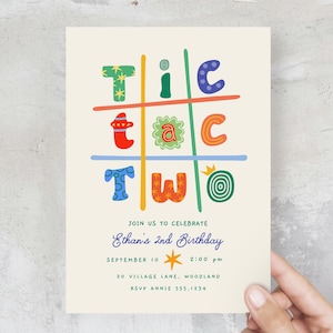 May include: A rectangular birthday invitation card on a cream background featuring a colorful tic-tac-toe grid with the text "tic tac two". Below, the text reads "JOIN US TO CELEBRATE Ethan's 2nd Birthday SEPTEMBER 10 2:00 pm 20 VILLAGE LANE, WOODLAND RSVP ANNIE 555-1234".