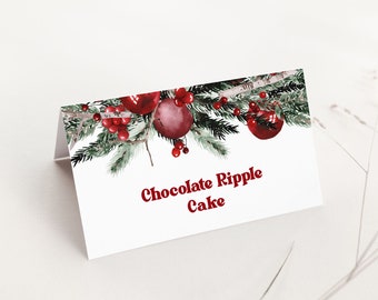 May include: A white, tent-style card with the text "Chocolate Ripple Cake" in red. The top edge features a watercolor design of red ornaments, berries, and evergreen branches. The card is on a white surface.