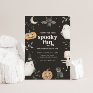 May include: A black and white Halloween party invitation with a spooky fun theme. The invitation features a ghost, a bat, a mummy, a pumpkin, and a black cat. The text on the invitation reads "Join us for some spooky fun. Taylor is turning one. Sunday, October 20 at 2:00pm. The Wilson House, 22 Green Avenue, Pine Lake. RSVP Emily at 555.5555."