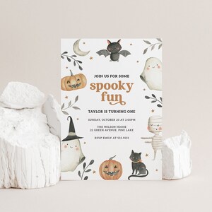 May include: A white invitation card with a spooky Halloween theme. The card features illustrations of a ghost, a bat, a pumpkin, a mummy, and a black cat. The text on the card reads "Join us for some spooky fun. Taylor is turning one. Sunday, October 20 at 2:00PM. The Wilson House, 22 Green Avenue, Pine Lake. RSVP Emily at 555.5555."