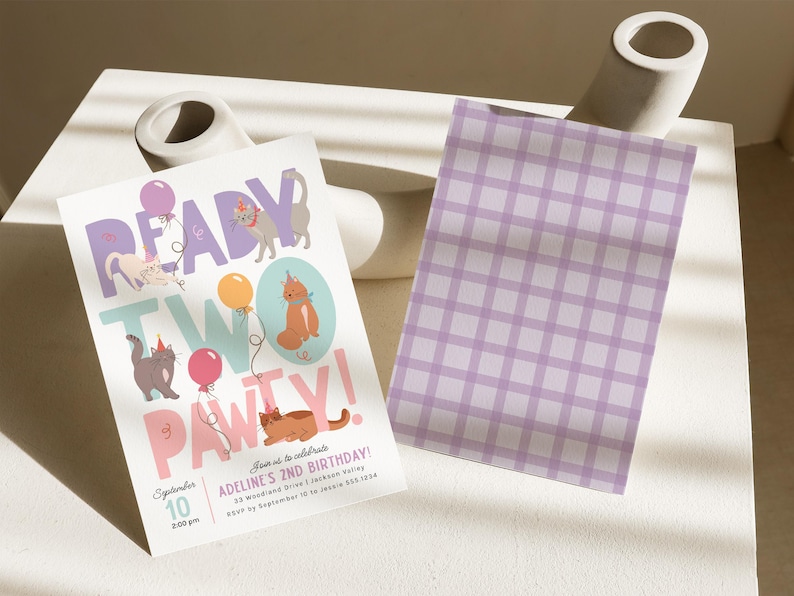 Op de afbeelding: Een roze en blauwe verjaardagsuitnodiging met de tekst "Ready Two Pawty!" en illustraties van katten en ballonnen. De uitnodiging is voor Adeline's 2e verjaardag en bevat de datum en tijd van het feest.