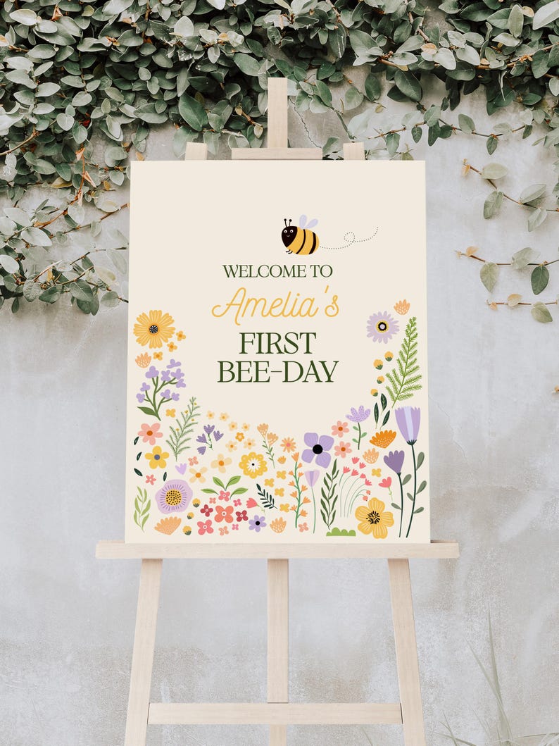 Puede incluir: Bienvenido a Amelia's First Bee-Day, un cartel con una abeja de dibujos animados y un borde floral. El cartel est&aacute; en un caballete de madera.