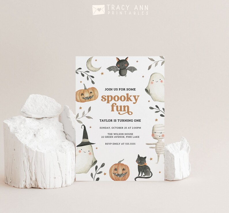 May include: A white invitation card with a spooky Halloween theme. The card features illustrations of a ghost, a bat, a pumpkin, a mummy, and a black cat. The text on the card reads "Join us for some spooky fun. Taylor is turning one. Sunday, October 20 at 2:00PM. The Wilson House, 22 Green Avenue, Pine Lake. RSVP Emily at 555.5555."