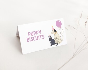 May include: A white folded card with the text "PUPPY BISCUITS" in purple. The card features illustrations of a spotted dog and a black cat wearing party hats, with a purple balloon. The design is whimsical and suitable for pet-themed products.