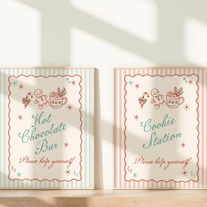 May include: Two framed signs with a vintage Christmas theme. One reads "Hot Chocolate Bar" and the other "Cookie Station." Both signs feature illustrations of gingerbread men, candy canes, and mugs. The signs have a striped background and a decorative border.