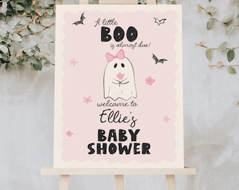 May include: A baby shower sign on an easel. The sign is light pink with the text "A little BOO is almost due!" and "welcome to Ellie's BABY SHOWER." A cartoon ghost with a pink bow is in the center, with bats and flowers around it.