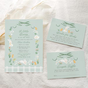 Pu&ograve; includere: Un invito a una festa di nascita di colore azzurro chiaro con un design di coniglietto e il testo "A little bunny is on the way!" L'invito include il nome "Elise Walker" e i dettagli della festa. Ci sono anche due biglietti per un libro e una lotteria di pannolini.