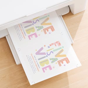 Pu&ograve; includere: Una stampante bianca che stampa colorati inviti per feste di compleanno. Gli inviti recitano "FESTIVE VIBE" in colori pastello, con il testo "Olivia's 5th Birthday". La stampante &egrave; su una superficie di legno chiaro.