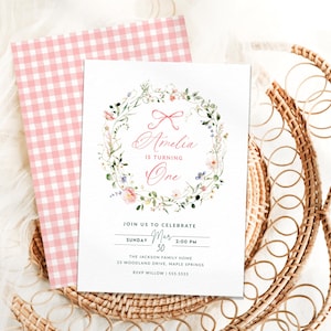 May include: A pink and white gingham background with a white card on top. The card has a floral wreath with a pink bow and the text "Amelia is turning One". The card also includes the text "Join us to celebrate Sunday Mar 30 2:00 PM The Jackson Family Home 23 Woodland Drive, Maple Springs RSVP Willow 555-5555".