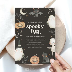 May include: A black and white Halloween party invitation with a spooky theme. The invitation features a ghost, a bat, a pumpkin, and a mummy. The text on the invitation reads "Join us for some spooky fun. Taylor is turning one. Sunday, October 20 at 2:00 PM. The Wilson House, 22 Green Avenue, Pine Lake. RSVP Emily at 555.5555."