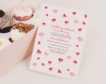 May include: A pink and white baby shower invitation featuring a watercolour design of hearts. The text reads "A little sweetheart is on the way" and includes the date, time, and location of the shower. The invitation also includes the name of the guest of honour, Hannah Johnson, and information about where she is registered.