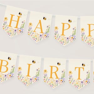 May include: A white banner with a floral pattern and yellow bees. The banner spells out "Happy Birthday" in yellow letters.
