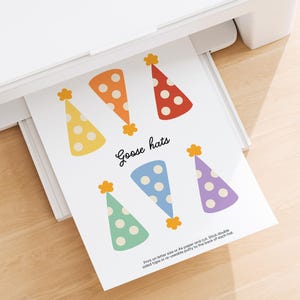 May include: A printed sheet of paper with six colorful party hats in yellow, orange, and red with white polka dots, and blue, green, and purple hats. The text "Goose hats" is written in cursive. The paper is coming out of a white printer.