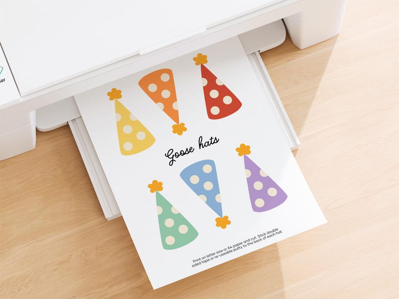 May include: A printed sheet of paper with six colorful party hats in yellow, orange, and red with white polka dots, and blue, green, and purple hats. The text "Goose hats" is written in cursive. The paper is coming out of a white printer.