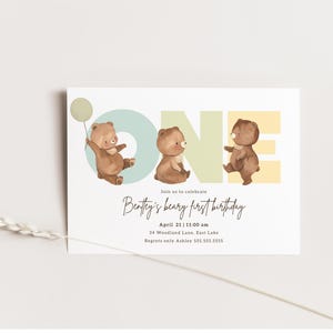 Puede incluir: Una invitaci&oacute;n azul claro, amarilla y verde con la palabra "ONE" en letras grandes. Tres osos de peluche marrones sostienen globos y est&aacute;n parados frente a las letras. El texto "Join us to celebrate Bentley's beary first birthday" est&aacute; escrito en cursiva debajo de las letras. La fecha, la hora, la direcci&oacute;n y la informaci&oacute;n de contacto se enumeran debajo del texto.