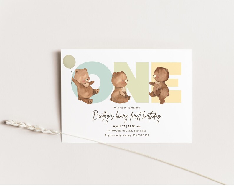 Puede incluir: Una invitaci&oacute;n azul claro, amarilla y verde con la palabra "ONE" en letras grandes. Tres osos de peluche marrones sostienen globos y est&aacute;n parados frente a las letras. El texto "Join us to celebrate Bentley's beary first birthday" est&aacute; escrito en cursiva debajo de las letras. La fecha, la hora, la direcci&oacute;n y la informaci&oacute;n de contacto se enumeran debajo del texto.