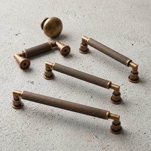 May include: A collection of antique brass hardware including one round cabinet knob and three linear drawer pulls. Each pull features a textured, knurled cylindrical grip with smooth, rounded mounting posts at both ends for attachment.