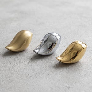 Può includere: Tre oggetti decorativi a forma di goccia disposti in fila. Il primo ha una finitura oro opaco, il secondo una finitura argento cromato lucido e il terzo una finitura oro lucido. Ogni pezzo presenta una forma liscia, curva e solida.