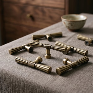 May include: A collection of six T-shaped cabinet pulls made of brushed brass. Each pull features a central cylindrical post with a ribbed texture and two flared, fluted horizontal arms extending from the center, creating a uniform metallic look.