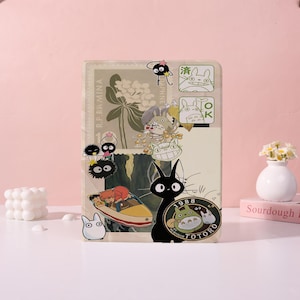 May include: A rectangular tablet case featuring a collage of Studio Ghibli characters including Totoro, Jiji, and soot sprites. The design incorporates vintage postage stamp motifs, a boat illustration, and the text 1988 My Neighbor Totoro.