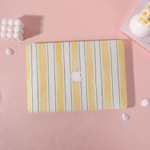 May include: A laptop with a yellow and white striped design. The laptop has a light pink Apple logo in the center. The stripes are vertical and have a watercolor effect. The background is light pink.