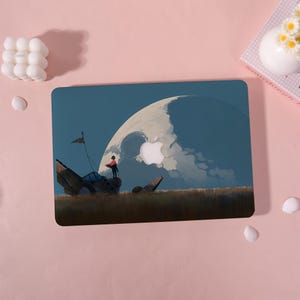 May include: A laptop case featuring a fantasy landscape with a large moon and a figure standing on a structure. The case has a dark blue background with a white Apple logo. The design includes a red flag and a person wearing a red cape.