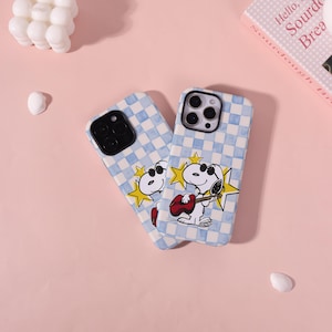 May include: Two phone cases featuring a light blue and white checkered pattern. Each case displays a cartoon dog wearing sunglasses and playing a red guitar, set against a yellow star graphic. The cases have black camera lens cutouts.