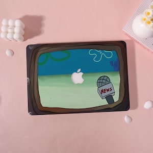 May include: A laptop case featuring a cartoon scene with a news microphone and the word "NEWS". The case has a brown border and a cartoon background with a white Apple logo. The case is on a pink surface.