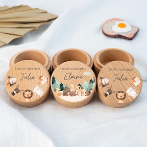 Può includere: Scatole in legno per fatine dei denti con coperchi. Ogni scatola è incisa con le parole "Tooth Fairy Box" e un nome. Le scatole sono decorate con illustrazioni di animali, tra cui un leone, una volpe e un cervo. I nomi "Julie" ed "Elaine" sono visibili.
