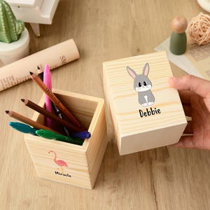 May include: Two small, unfinished wooden boxes. One contains colored pencils and pens, and features a pink flamingo with the word "Miracle". The other box has a cartoon bunny and the name "Debbie".