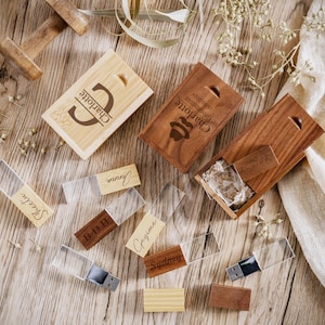 May include: Wooden USB flash drives and cases with personalized engraving. The flash drives have clear plastic covers and are engraved with names. The wooden cases are rectangular and feature the name "Charlotte" and other names.
