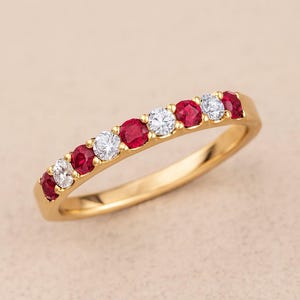Peut inclure: Une bague en or avec une rangée alternée de pierres précieuses rouges et blanches. La bague présente une rangée de rubis et de diamants ronds sertis dans une monture en or poli. Les pierres sont espacées uniformément.